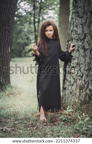 A little girl in a witch costume in a forest near a tree, Halloween concept