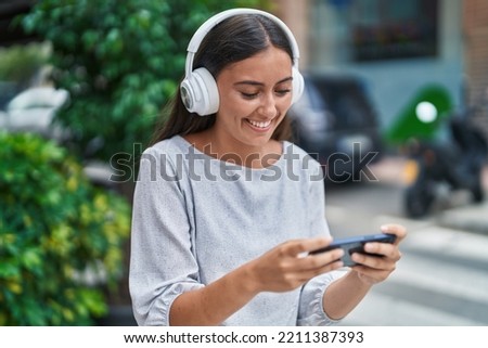 Young beautiful hispanic woman smiling confident playing video game at street