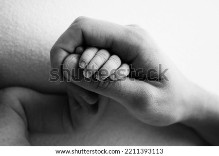 The hand of a sleeping newborn in the hand of parents, mother and father close-up. Tiny fingers of a newborn. The family is holding hands. Black and white macro photography Concepts of family and love