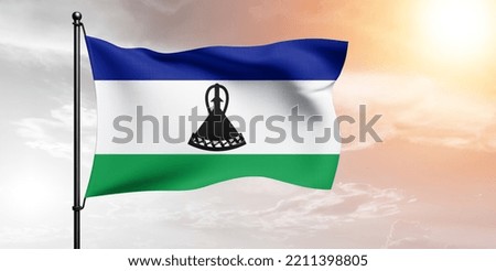 Lesotho national flag cloth fabric waving on beautiful grey sky.