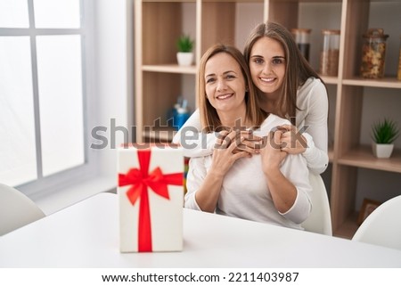 Two women mother and daughter hugging each other surprise with gift at home