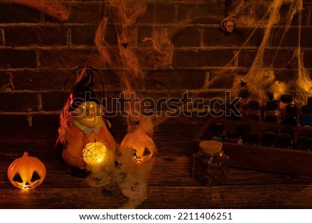 witch illuminated from inside with pumpkins, spiders, illuminated spider web, potion pots, brick backdrop, wooden table and text space
