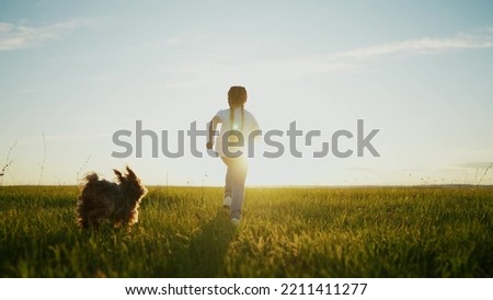 little girl child and dog a run in the park. happy family kid dream holiday concept. girl child silhouette view from the back runs with a pet dog on the grass in the summer in sunset the park at