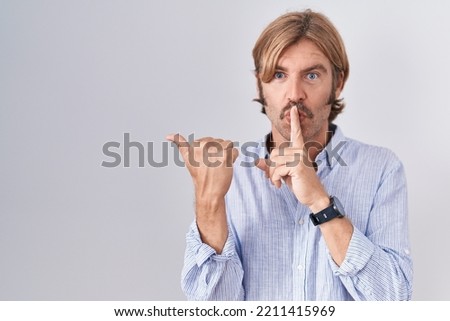 Caucasian man with mustache standing over white background asking to be quiet with finger on lips pointing with hand to the side. silence and secret concept. 