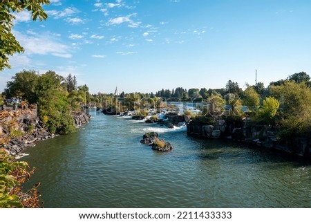 Beautiful view of Snake river flowing near temple in Idaho falls. Picturesque scenery of flowing water amidst rocks and plants with sky in background. Scenic tourist attraction during summer.