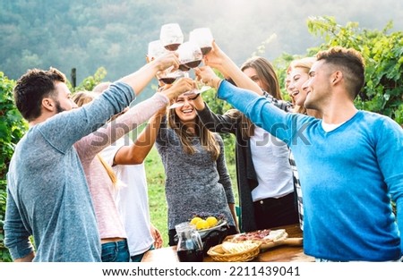 Fancy friends enjoying harvest time together drinking at farm house country side - Beverage life style concept with young people toasting red wine glasses at italian vineyard - Bright vivid filter