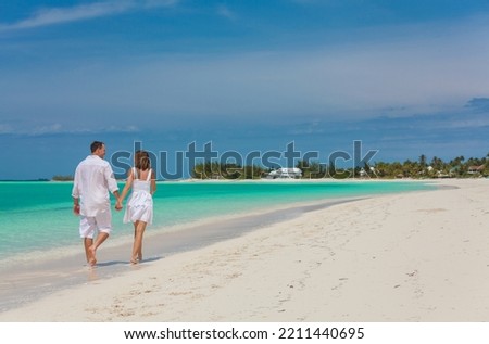 Romantic male and female Caucasian American couple walking by the coast together on tropical beach for relaxation  Royalty-Free Stock Photo #2211440695