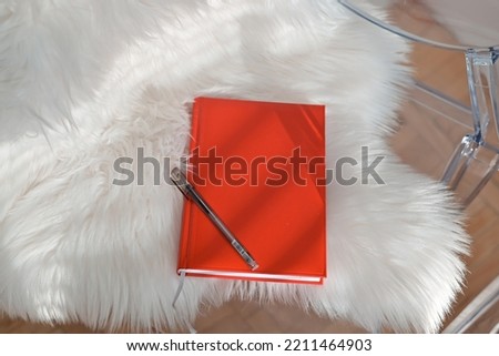 Book in red cover on white background. Red colored note paper diary and a black colored ball point pen placed together.