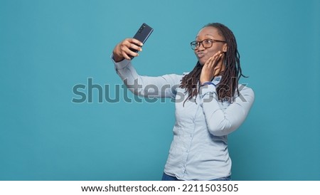 Cheerful happy woman taking pictures on smartphone app, having fun with mobile phone camera to take funny selfies in studio. Natural confident person photographing over blue background.