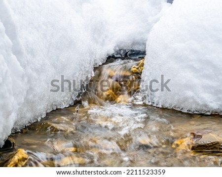 Minimalist abstract picture of a mountain stream flowing beneath the white frozen snow.