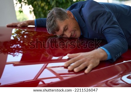 Happy man in car showroom hugging car hood