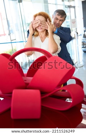 Man closed woman's eyes his palms, he gives her red car