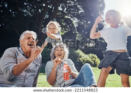 Grandparents, bubbles and children play in park happy together for fun, joy and outdoor happiness. Retired, smile and excited elderly senior couple, girl grandkids and love playing outside in nature Royalty-Free Stock Photo #2211548823