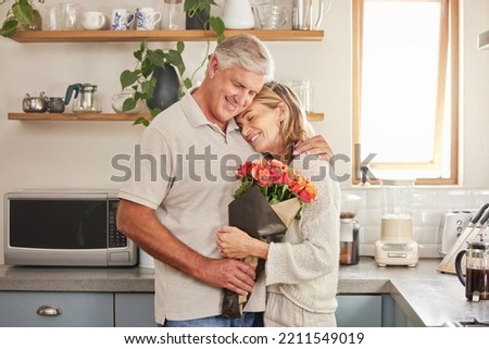Flower bouquet, hug and senior couple with smile for celebration of marriage in kitchen of their house. Elderly man and woman giving roses as gift while hugging for love, anniversary or birthday