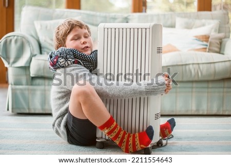 Child enjoy heat radiator. Boy hug warm battery. Heating of housing during the energy crisis in the winter cold season. Restrictions and savings of gas and electricity. Heat. Comfort. Royalty-Free Stock Photo #2211554643