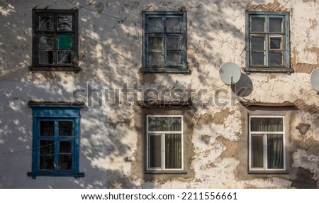Windows on an old shabby concrete wall. An old Soviet building in the Kazakh city of Pavlodar. Window with wooden frame. Round telephysic satellite dish. Copyspace