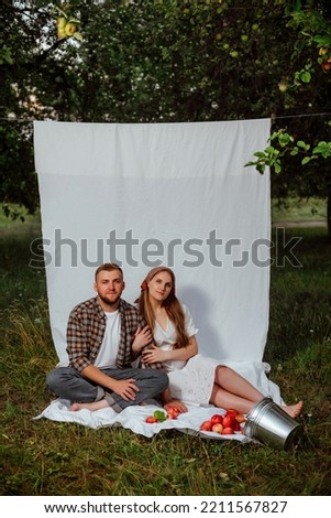 a pregnant girl in a white dress and her husband in a shirt pose on a white background in the garden