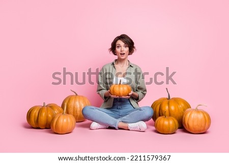 Full size portrait of astonished person sit hold pumpkin open mouth look camera isolated on pink color background