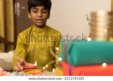Young boy, kid, dressed up in ethnic lighting diya or lamp with smile expression pose for photo with family in background celebrating diwali Hindu festival Laxmi poojan
