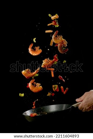 Crop anonymous male chef tossing food in frying pan while preparing delicious prawns and vegetables against black background Royalty-Free Stock Photo #2211604893