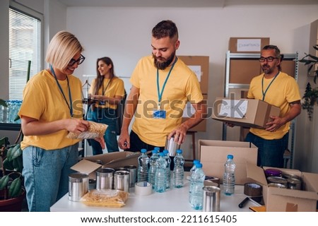 Volunteers working at charity organization and wearing yellow t shirt while packing food grocery in donations box. Volunteering, social help for poor and needy. Working together as a team. Royalty-Free Stock Photo #2211615405