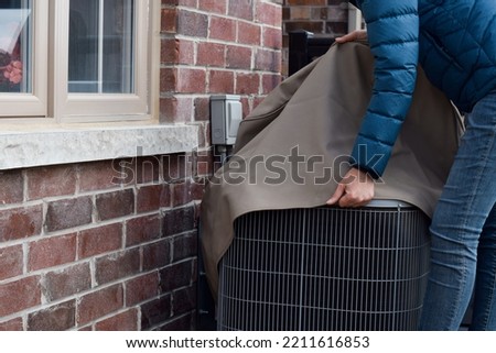 Woman putting cover on air conditioner unit outside the house Royalty-Free Stock Photo #2211616853