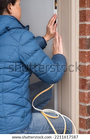 Woman attaching isulation strip to front door of the house Royalty-Free Stock Photo #2211617587