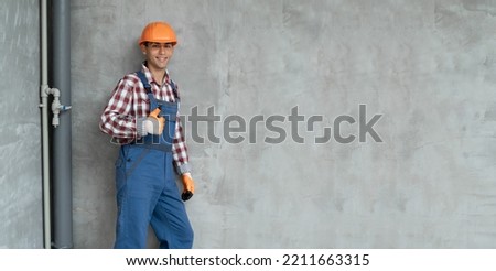 happy smiling male worker or builder in yellow helmet and overall showing thumb up over gray background. Banner. profession, construction and building concept