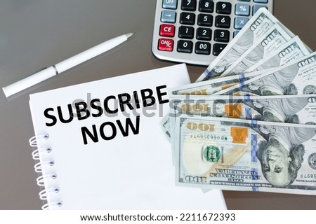 SUBSCRIBE NOW inscription on notepad next to pen, calculator and dollar money
