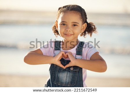 Girl at beach make heart sign with hands, happy and smile against blurred nature background. Young female child with expression of happiness, makes love icon, gesture with fingers by the ocean or sea