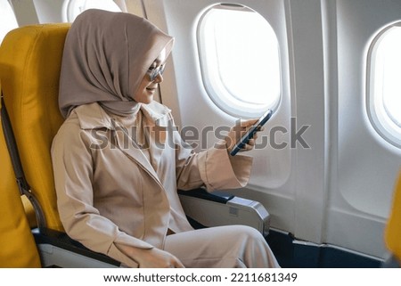 Beautiful muslim woman using mobile phone in airplane.