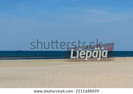 Liepaja, big sign on the coast. Big letters in sunny beach. A ship on the horizon.