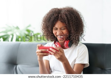 Beautiful young woman playing game on her mobile phone in her living room on sofa at home happily and enjoying her vacation.