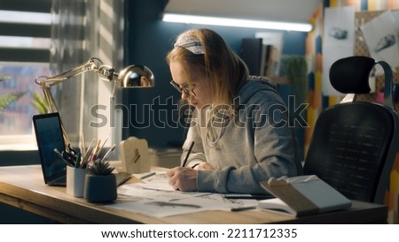 Young female artist draws pencil sketches on a sheet of paper. The illustrator creates a storyboard looking at the laptop screen. Storytelling concept. Video editing.