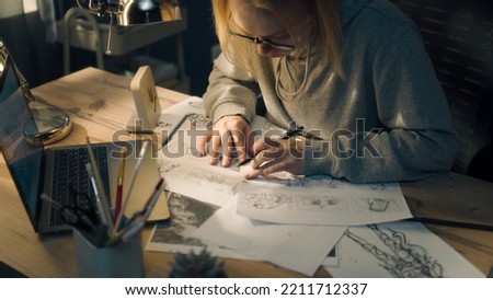 Young woman works on a storyboard in a home based design studio. A laptop and stationary jar on the table. Woman draws sketches as a roadmap for the video. Pre-production.
