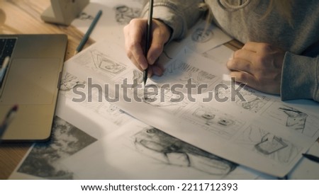 Closeup hands of a woman making pencil sketches. Working on a storyboard in a home based design studio. Woman drawing sketches as a roadmap for the video. Story telling. Royalty-Free Stock Photo #2211712393