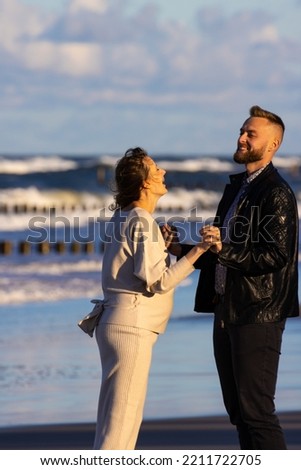 A handsome man and his pregnant wife dance and hug during a sunset on the beach; pregnant love; adoration of a pregnant woman