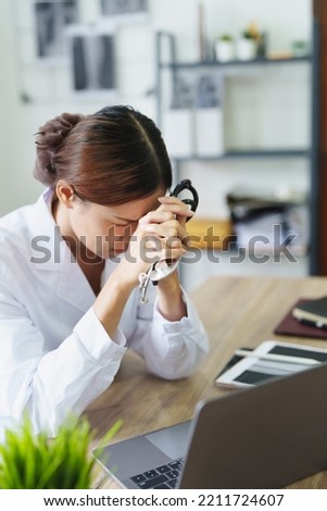 An Asian female doctor uses a computer while showing concern about patient information.