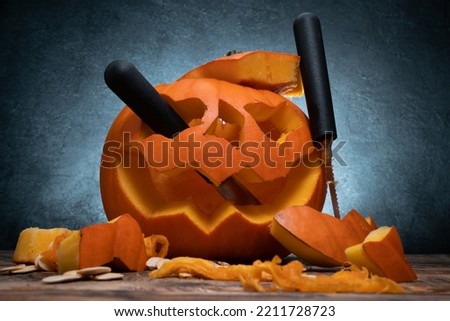 Carved Halloween pumpkin, Jack Lantern head with carving tools. Spooky Jack-o'-lantern face cut out with saw knife blade and scoop gutter carvers. Seeds and pieces scattered around.
