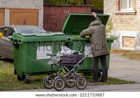 homeless guy looking for food in green garbage cans on the street. life on the street. Lifestyle of a tramp, living in the streets Royalty-Free Stock Photo #2211733887