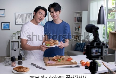 Young Asian male couple blogger influencer vlogger shooting video in kitchen. LGBT  gay couple live- streaming cooking class from home.