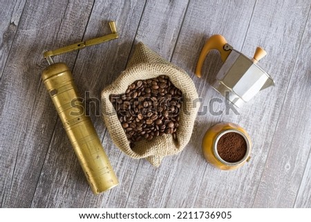 Decorated scene with coffee grinder, jute sack filled with roasted coffee beans and moka pot Royalty-Free Stock Photo #2211736905