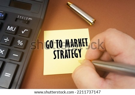 Business concept. A calculator lies on a brown surface, a hand with a pen makes an inscription on a sticker - Go to market strategy
