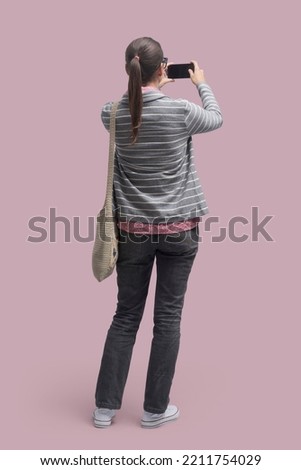Young casual woman taking pictures with her smartphone and sharing online, full-length portrait