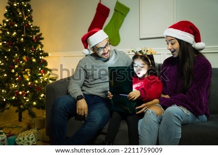 Surprised little girl opening an exciting present with her parents during christmas night at home