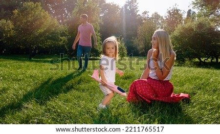 Happy and excited mommy and her little daughter running in front of the camera through the grass with a airplane in hands