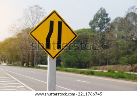 Yellow traffic square shaped left narrow lane sign at rural road Thailand to aware driver know Road narrows on left side ahead. Concept: Warning traffic sign for transportation.                       