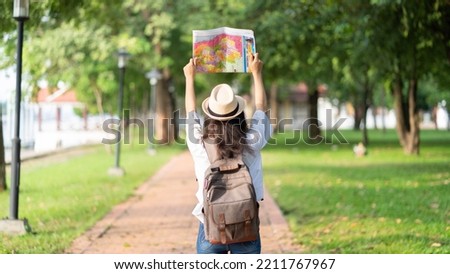 Young female traveler with hat and backpack traveling with paper map on the garden in vacations