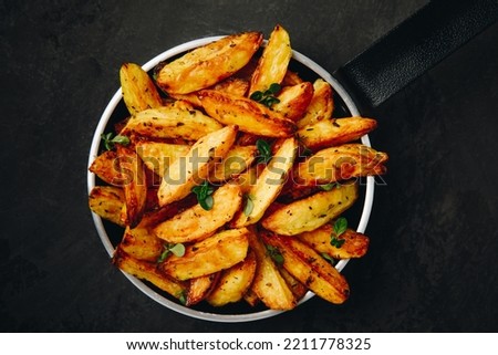 Roasted potatoes. Baked potato wedges in frying pan on dark stone background. Top view with copy space. Royalty-Free Stock Photo #2211778325