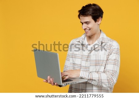 Young smiling happy copywriter freelancer caucasian man 20s wearing white casual shirt hold use work on laptop pc computer isolated on plain yellow background studio portrait. People lifestyle concept